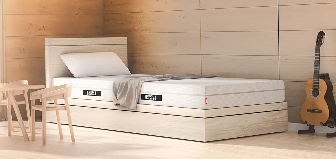 Matelas BODYGUARD® sur un lit en bois clair dans une chambre cosy avec guitare et coin repas.
